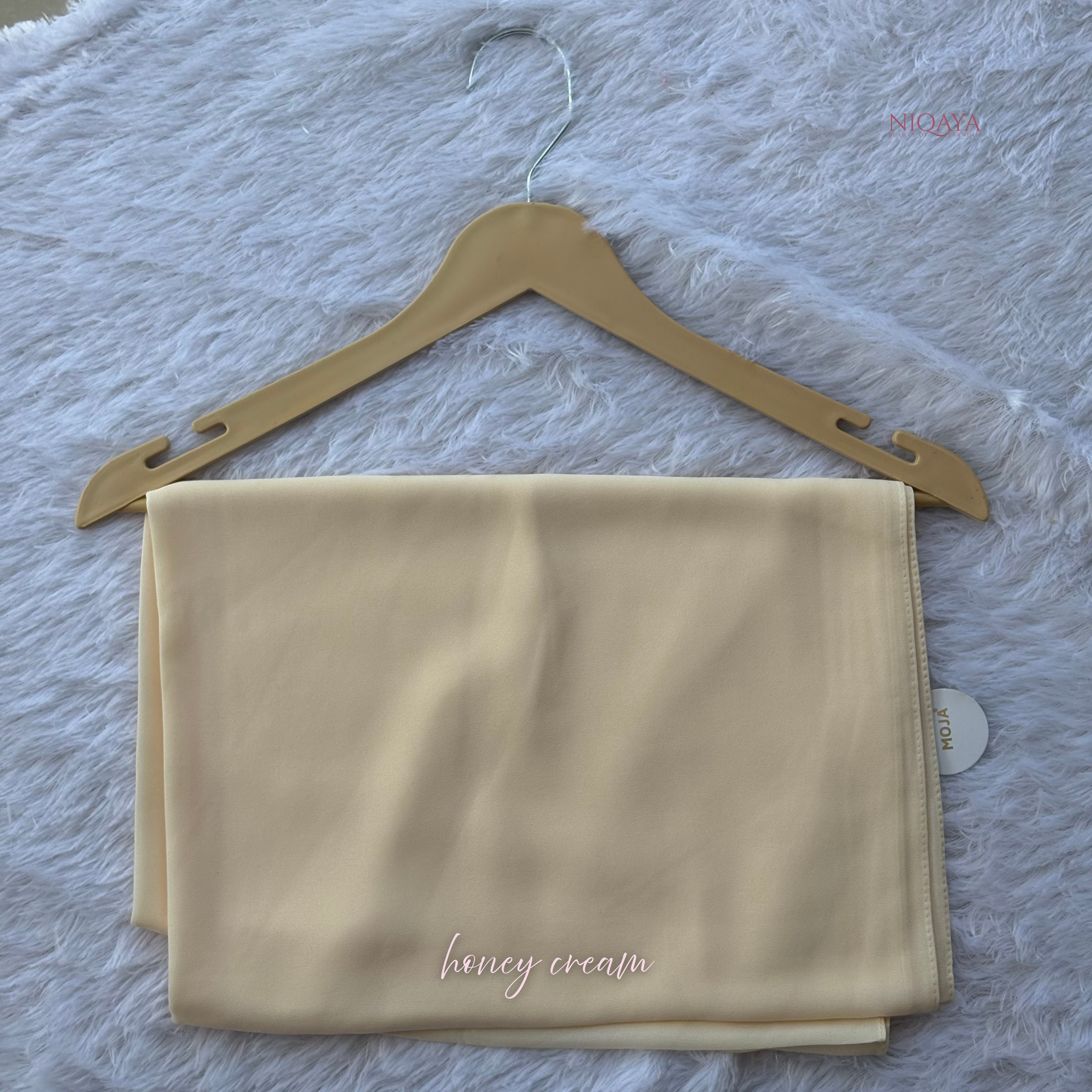 Beige fabric with 'honey cream' text on a hanger against a textured gray background