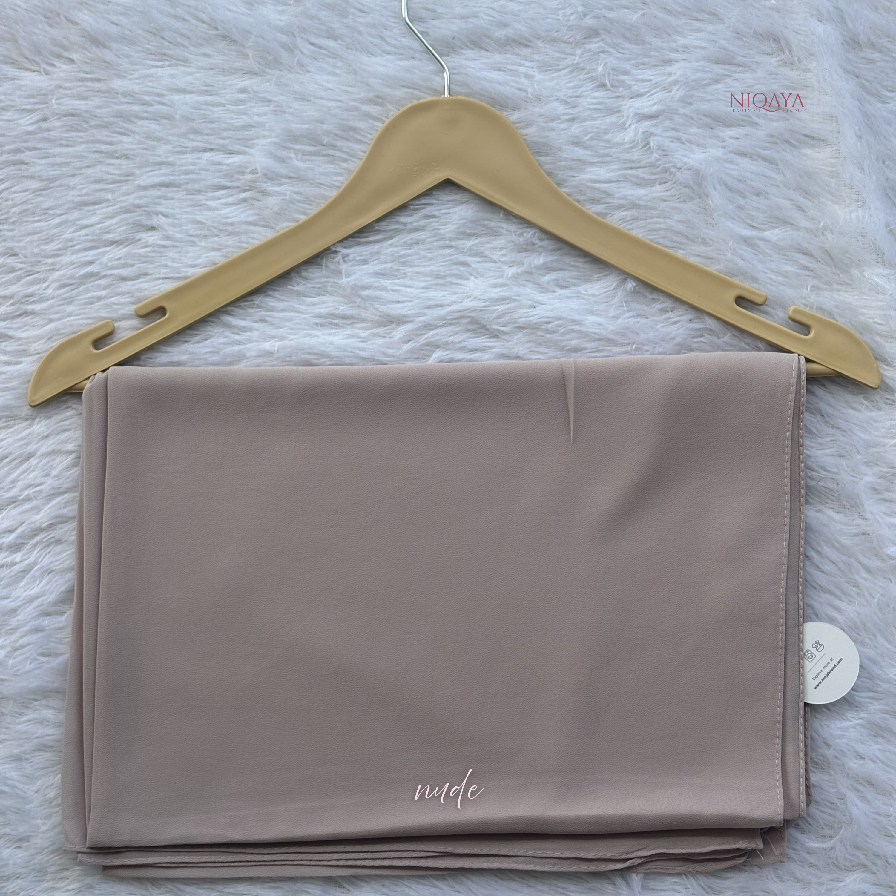 Folded nude fabric on a gold hanger with 'Nida' branding on a textured white background