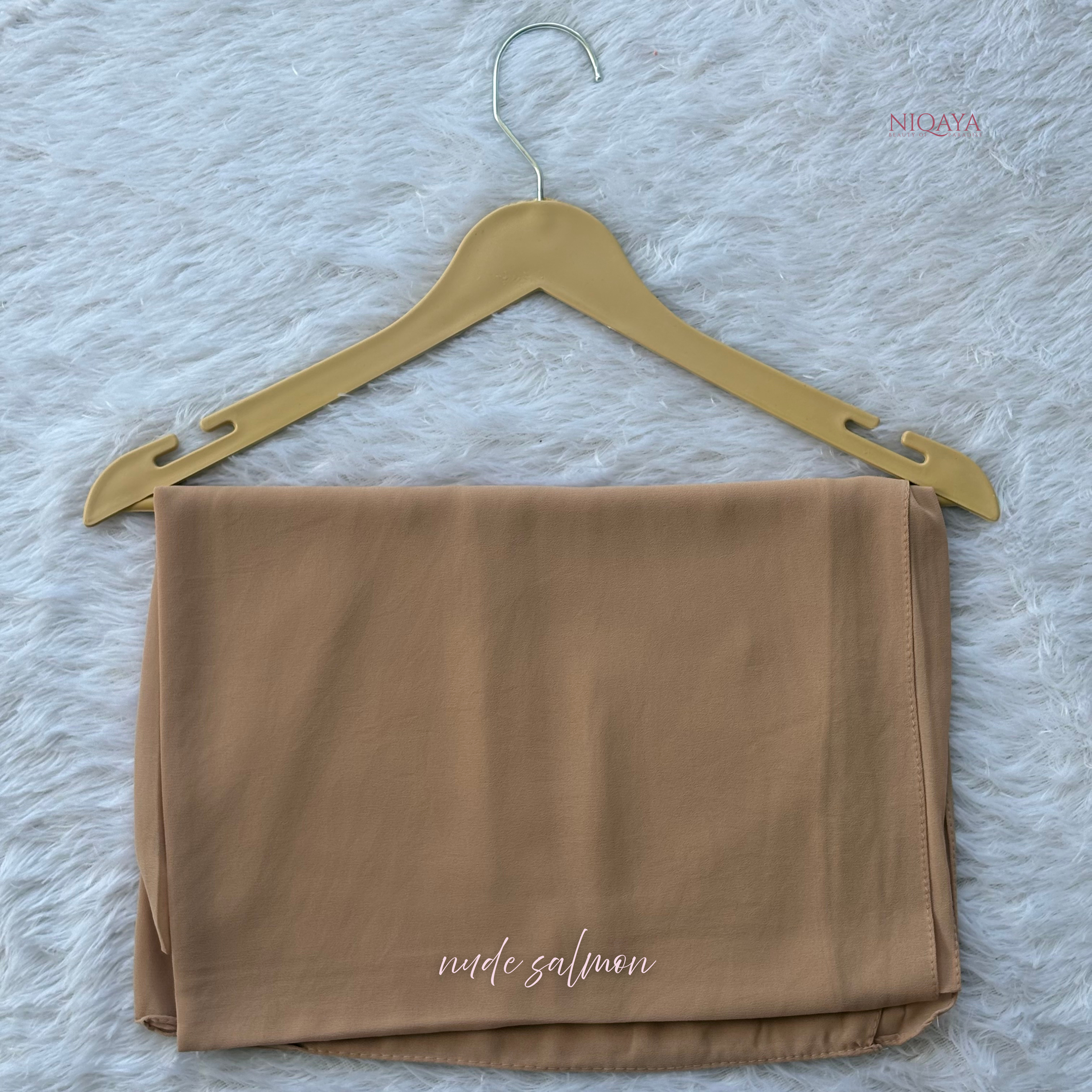 Folded nude salmon fabric on a gold hanger against a textured white background