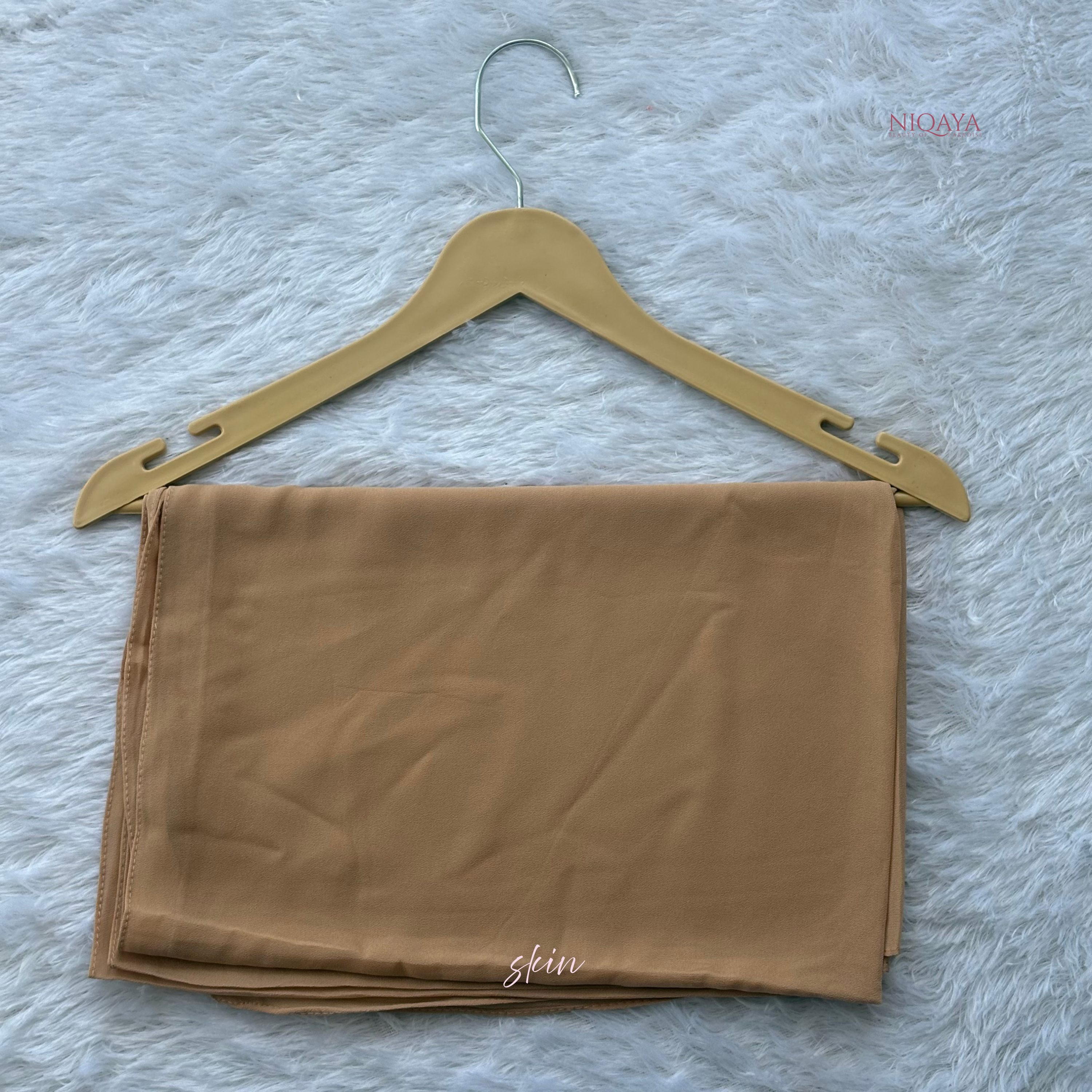 Folded beige fabric on a gold hanger against a textured white background