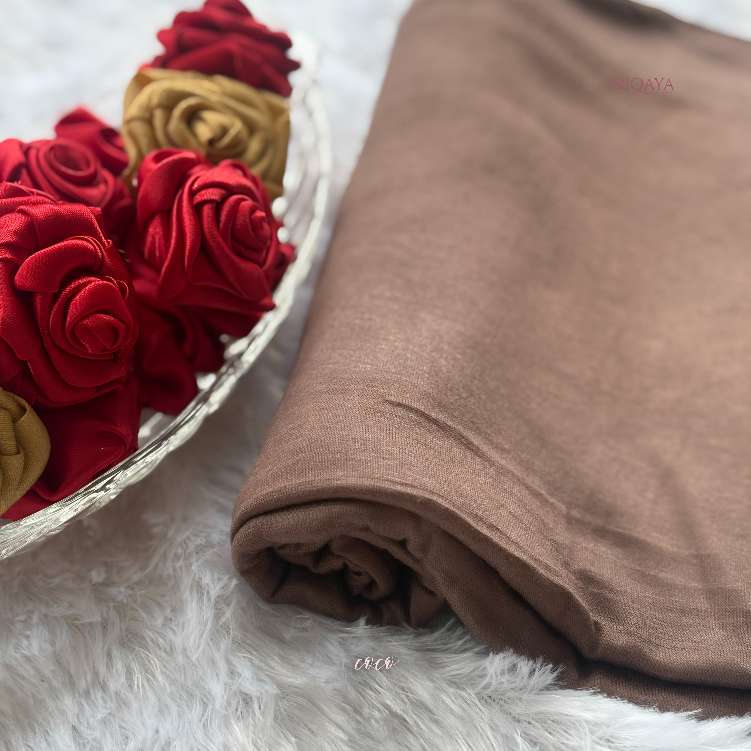 Brown fabric roll next to red and gold flowers on a white surface