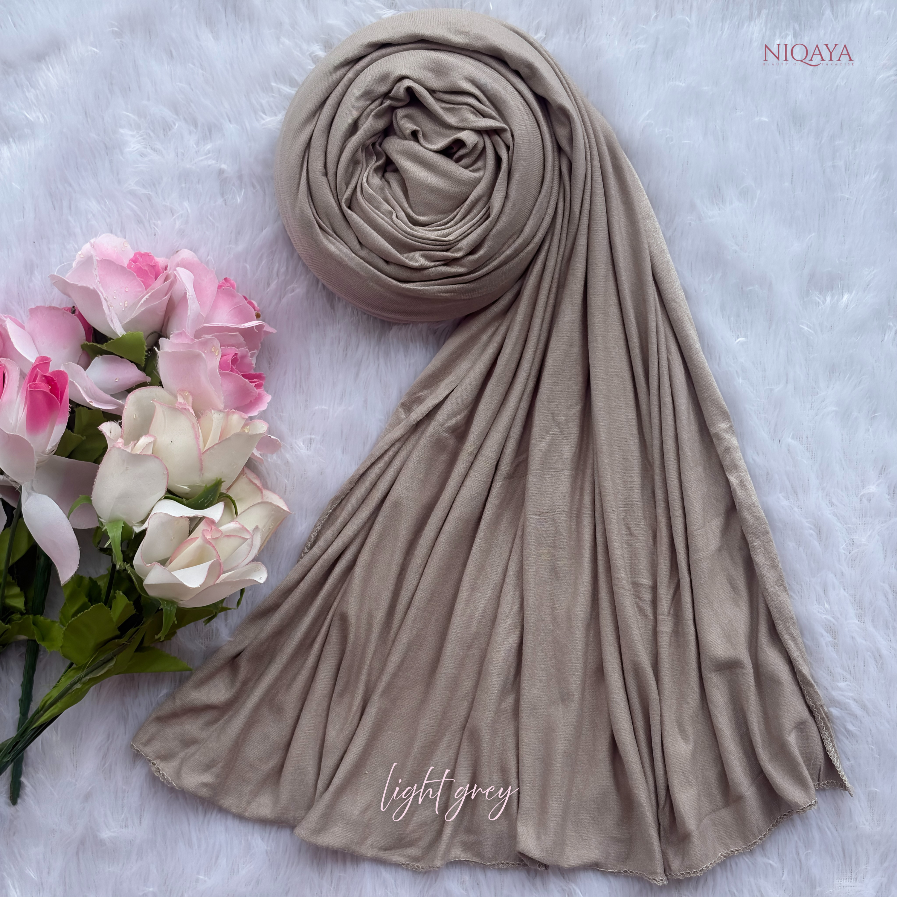 Light gray hijab with flowers on a textured white background, featuring the brand 'NIOQAYA'.