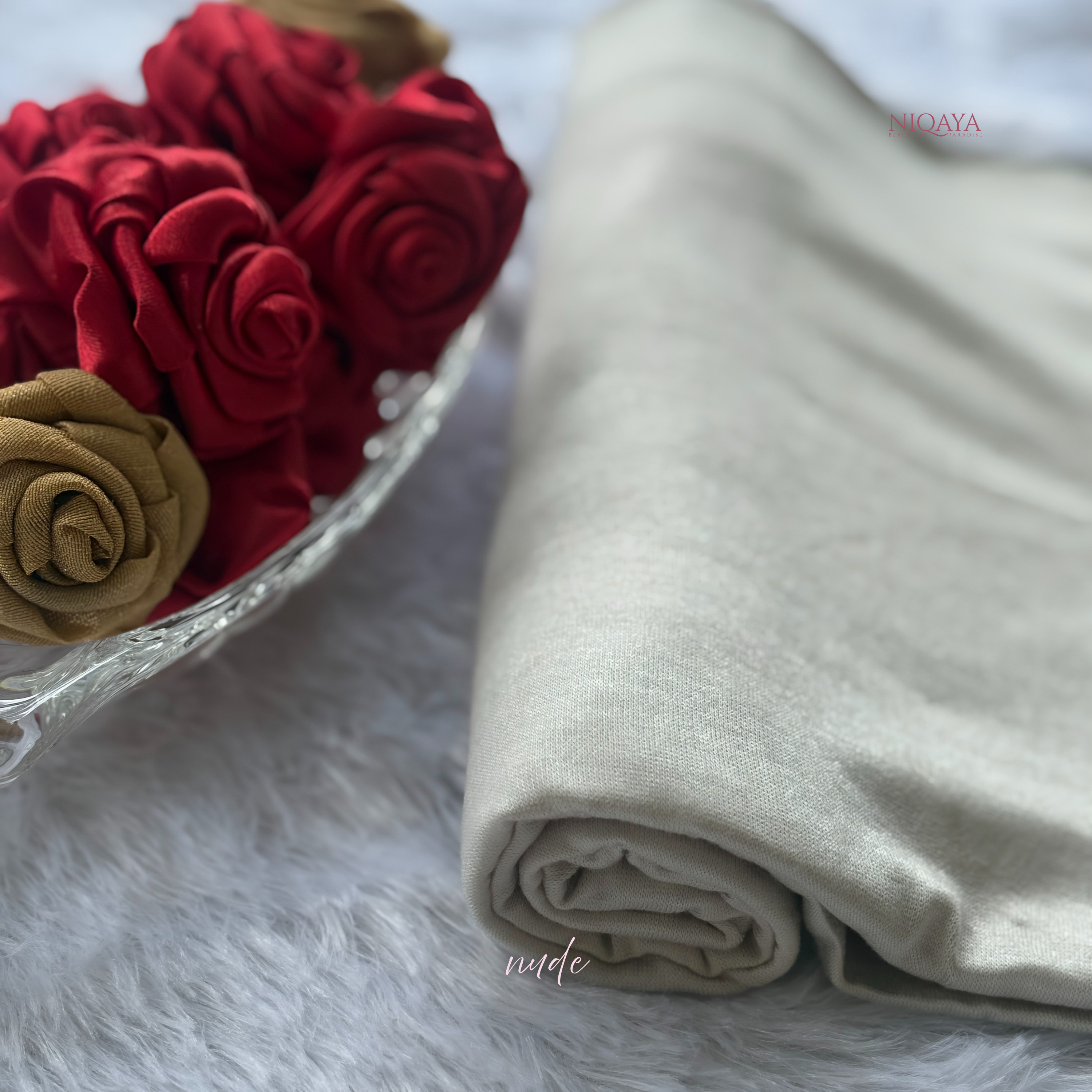 Folded beige fabric next to red and gold artificial flowers on a white surface