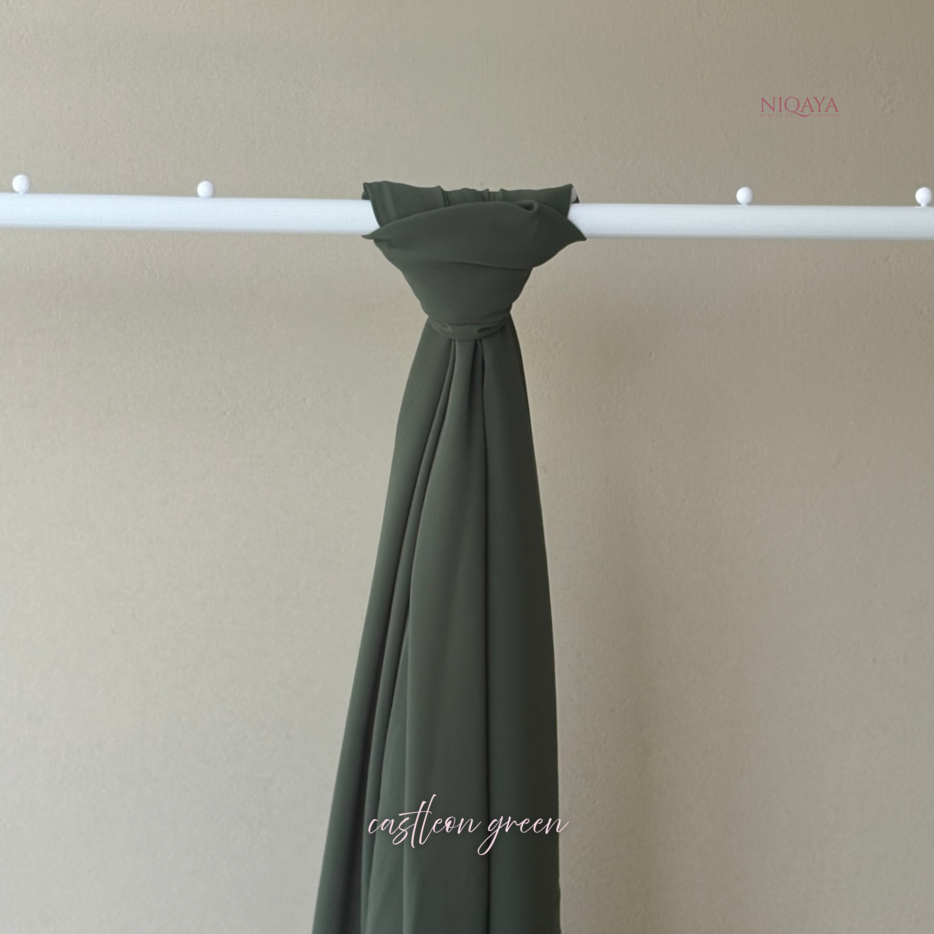 Green fabric draped over a white rod against a beige background, with 'NIQAYA' branding.