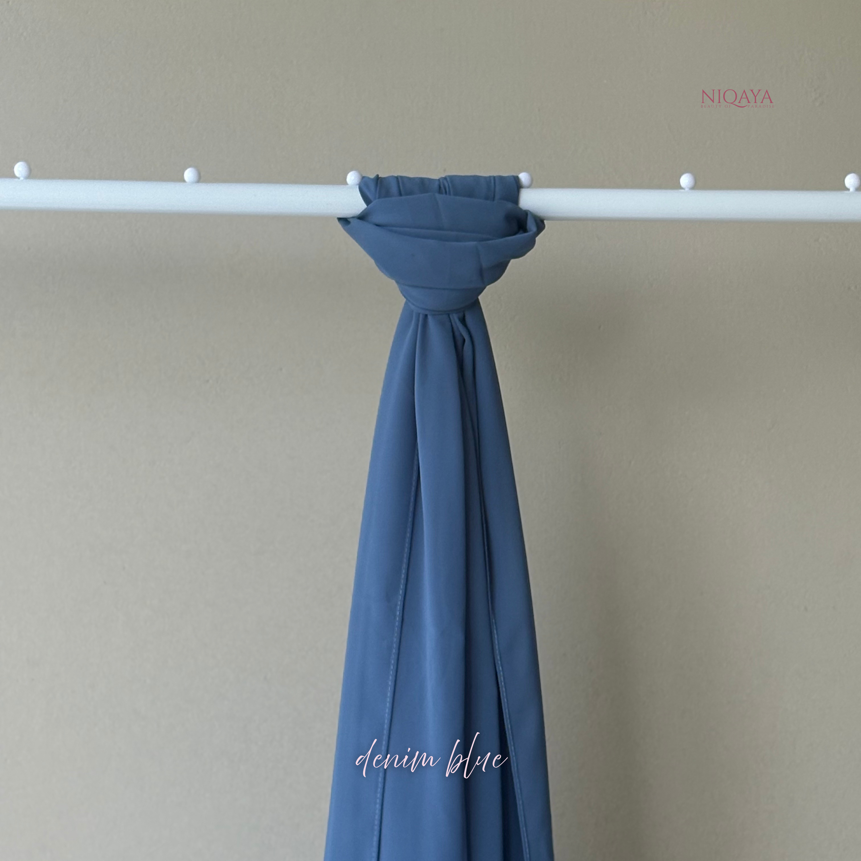 Blue fabric draped over a white rod against a beige wall with 'Niqaya' branding.