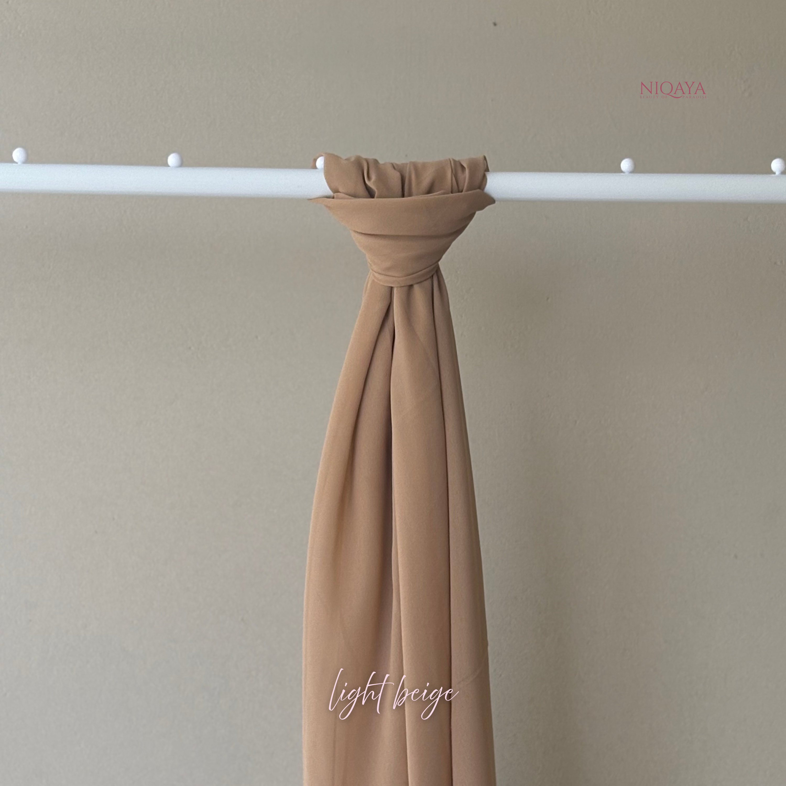 Light beige fabric draped over a white rod against a beige background, with 'Niqaya' branding.