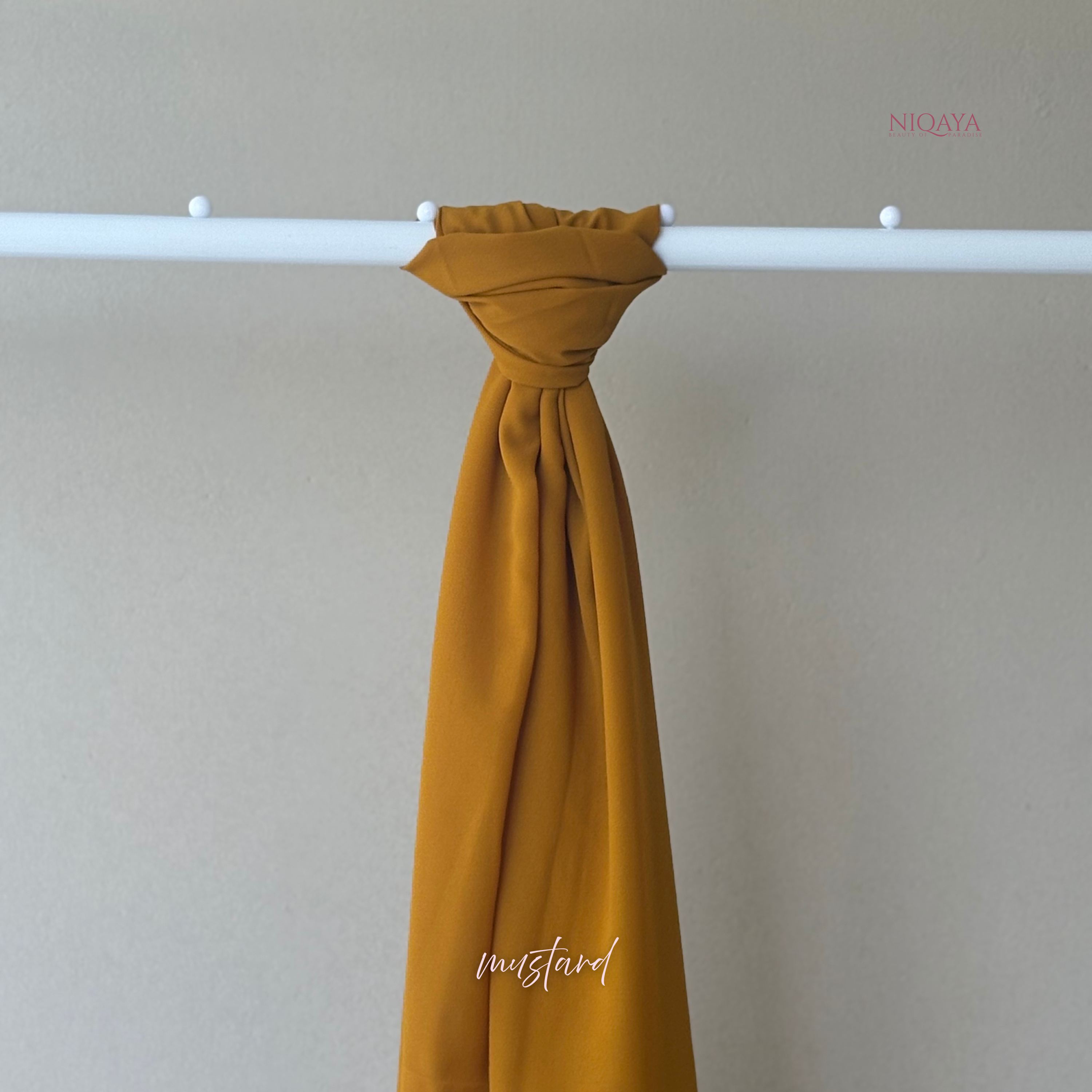 Mustard yellow fabric draped over a white rod against a beige background