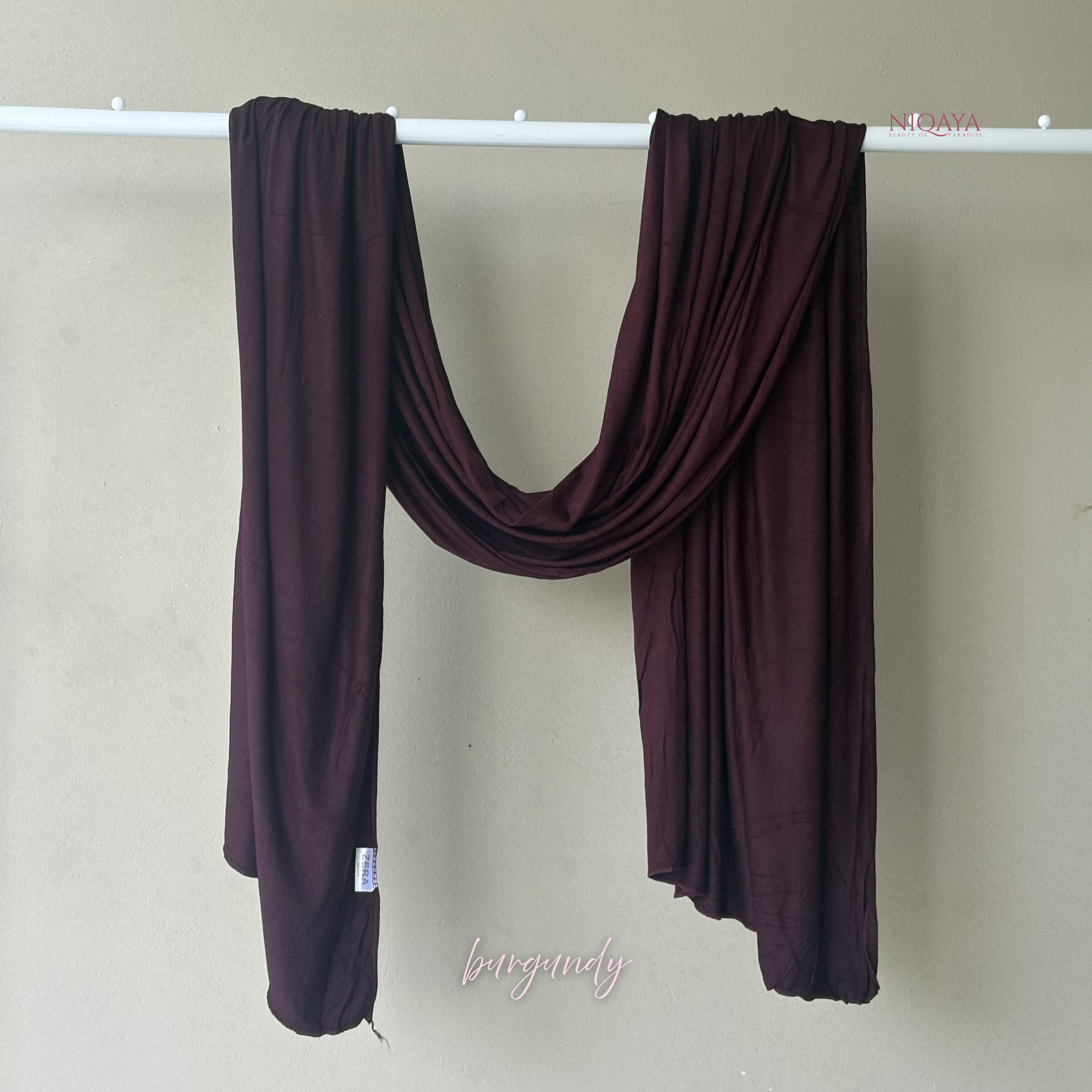 Dark purple scarf draped over a white rod against a beige wall.