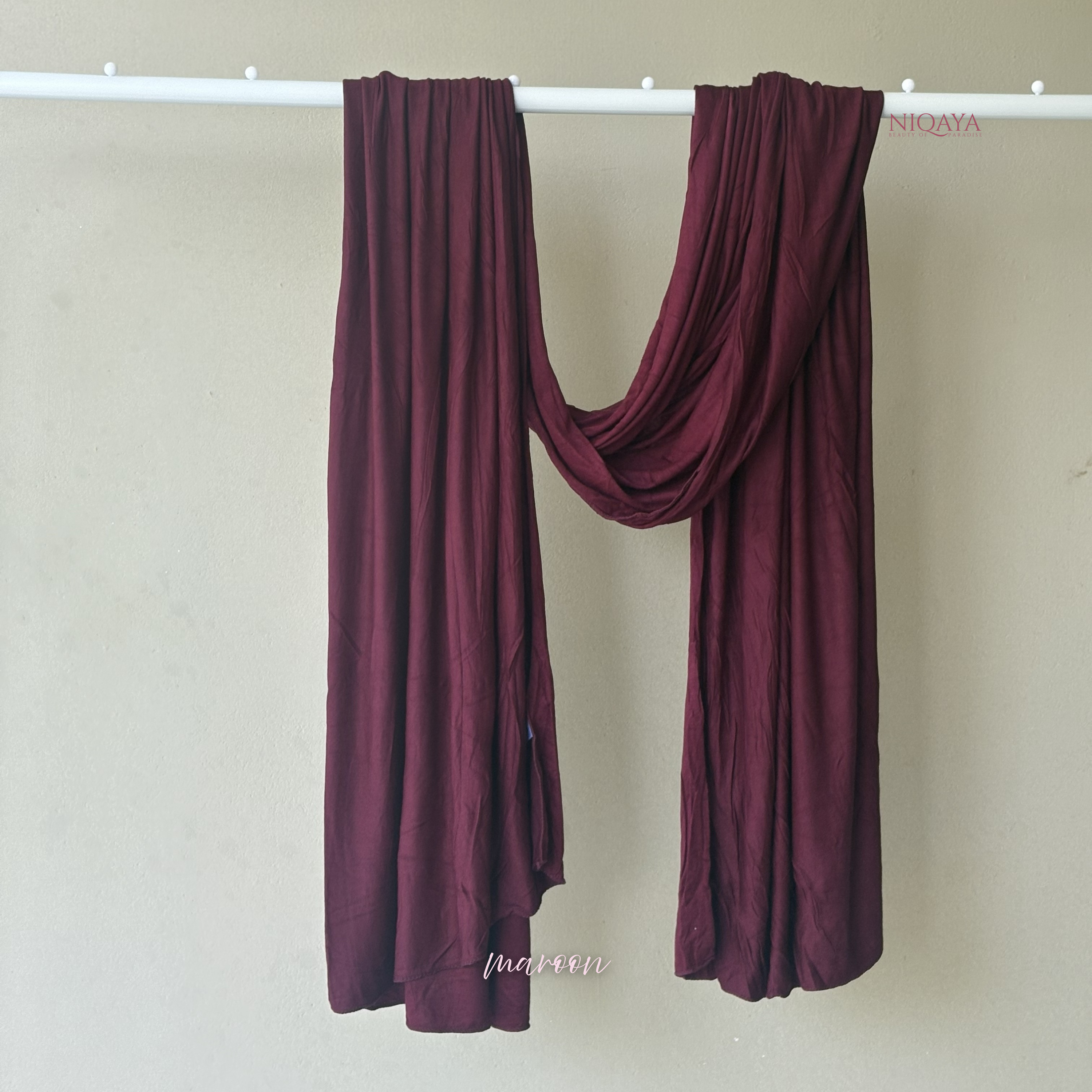 Burgundy scarf draped over a white rod against a beige wall