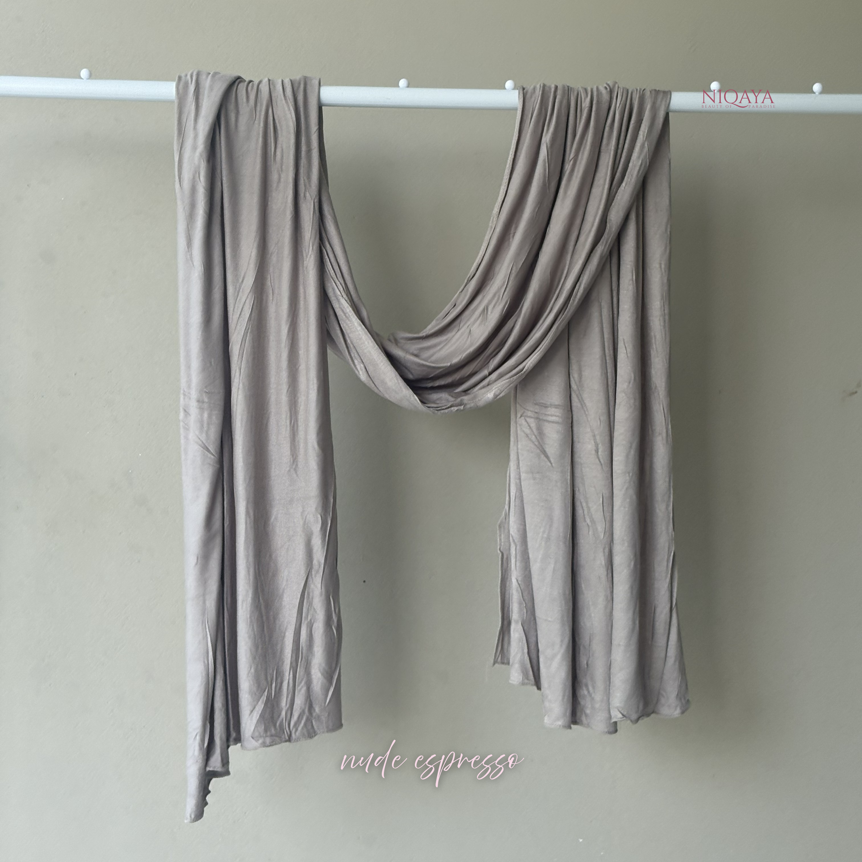 Gray scarf draped over a white rod against a beige wall with 'Nida Espresso' branding.