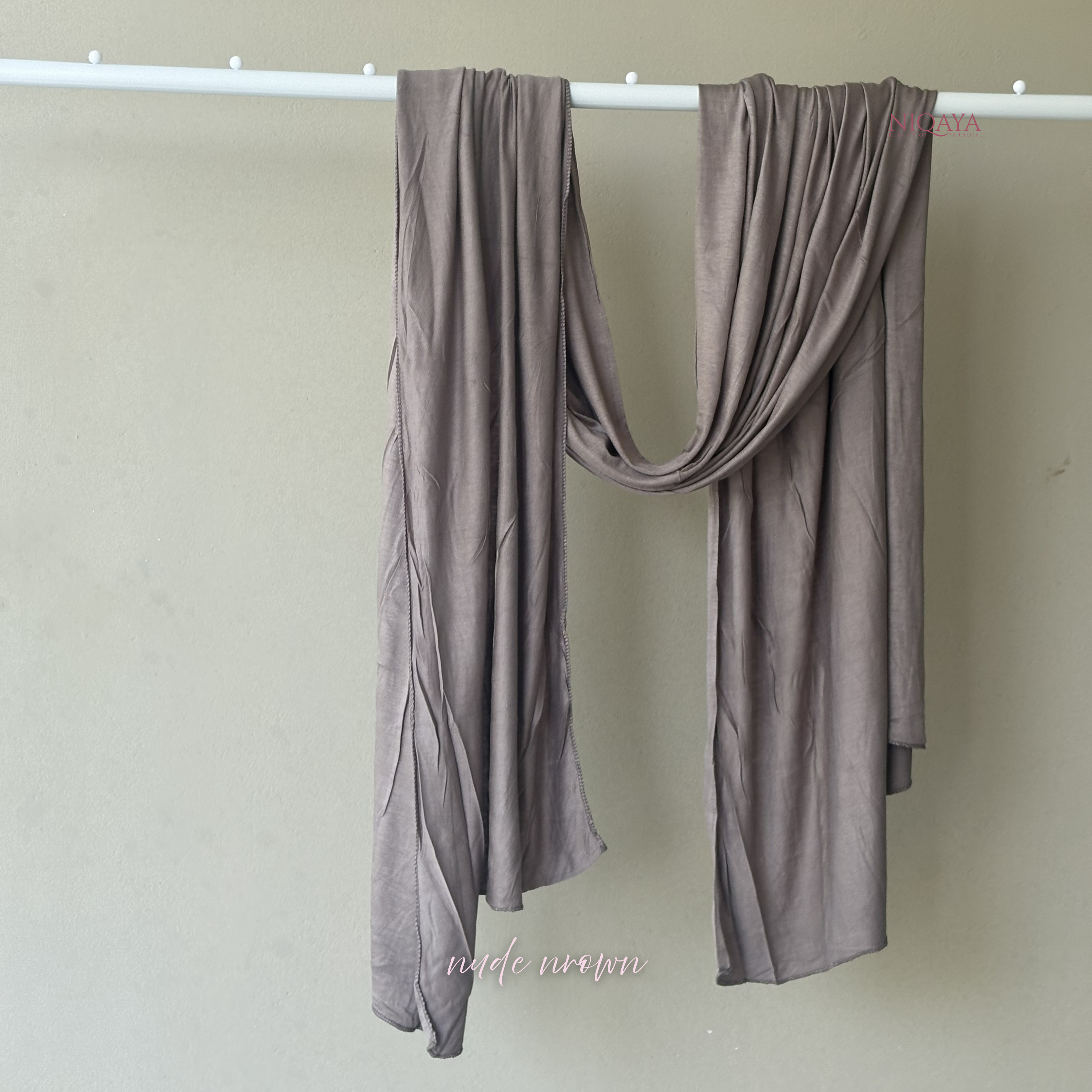 Brown scarf draped over a white rod against a beige wall