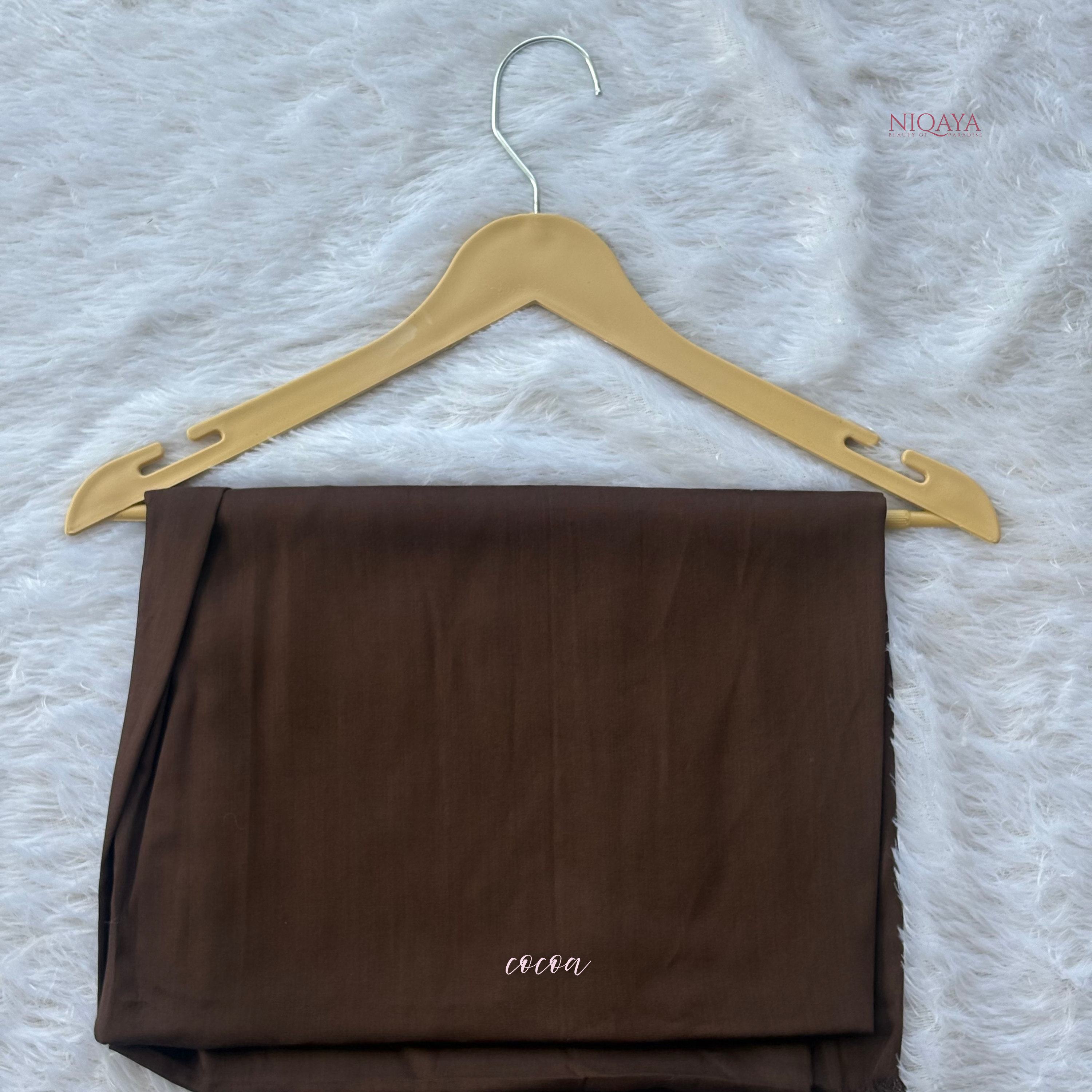 Brown fabric on a gold hanger with 'NIOQAYA' branding on a textured white background